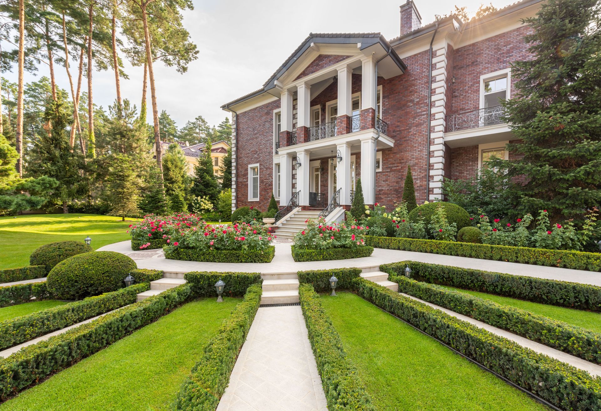 Well-kept formal garden with clipped hedges, lawn panels and rose beds in front of a brick house